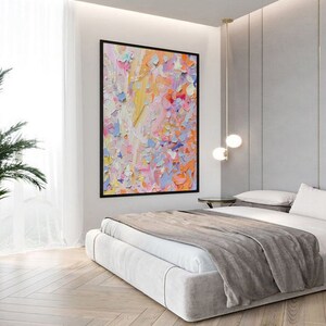 May include: A large abstract painting with a black frame hangs above a bed. The artwork features a textured, colorful palette of orange, pink, yellow, and blue. The bedroom has a modern design with a light-colored bed and wooden floors.