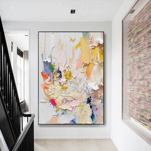 Op de afbeelding: Abstract schilderij met een witte achtergrond en kleurrijke penseelstreken in tinten roze, geel, blauw en groen. Het schilderij heeft een textuur en gelaagde uitstraling.