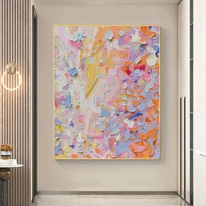May include: Abstract oil painting with a gold frame. The artwork features a textured surface with a palette of colors including yellow, pink, orange, blue, and white. The brushstrokes are visible, creating a dynamic and vibrant composition.