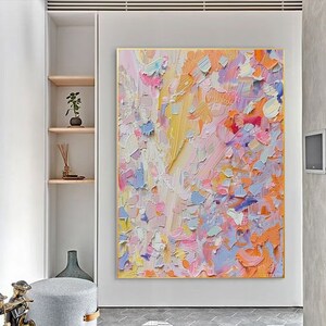 May include: Large abstract painting with a gold frame. The artwork features a textured surface with a palette of pastel colors, including pink, yellow, blue, and orange. The brushstrokes create a dynamic and expressive composition.