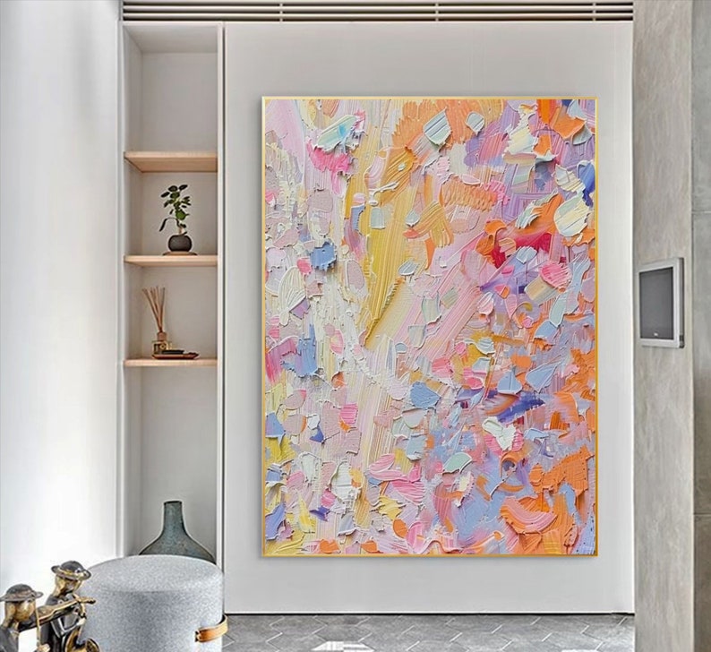 May include: Large abstract painting with a gold frame. The artwork features a textured surface with a palette of pastel colors, including pink, yellow, blue, and orange. The brushstrokes create a dynamic and expressive composition.