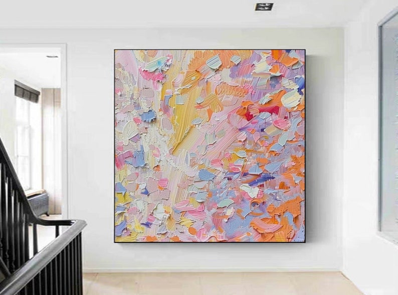 May include: Abstract oil painting with a textured surface. The artwork features a vibrant palette of colors, including yellow, pink, orange, and blue. The painting is displayed in a black frame, adding a modern touch to the colorful composition.