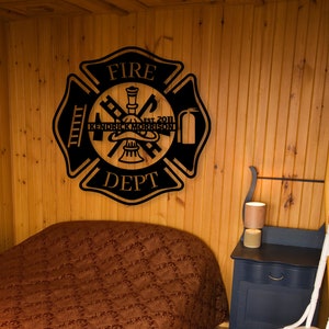 May include: Black metal fire department sign with the words "FIRE DEPT" and "EST. 2011" and the name "KENDRICK MORRISON" in the center. The sign is mounted on a wooden wall.