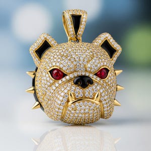 May include: A gold-colored pendant in the shape of a bulldog's head, encrusted with small, clear gemstones. The bulldog has red eyes, black accents, and gold-colored spikes around its neck. The pendant has a gold bail.