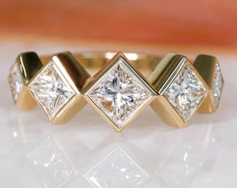 Puede incluir: Un anillo de banda de oro con cinco diamantes de forma cuadrada engastados en la banda. Los diamantes son transparentes y tienen un corte brillante.