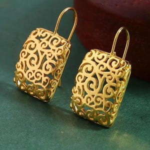 May include: A pair of gold-toned dangle earrings with a square-shaped design featuring intricate filigree details.