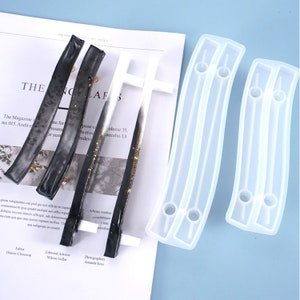 May include: An assortment of resin molds and finished resin pieces. The molds are clear, curved, and have holes for hardware. The finished pieces are black, white, and gold, with a curved shape. The items are on a magazine page.