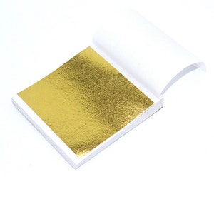 May include: A gold leaf sheet in a white paper booklet. The gold leaf is very thin and has a textured surface.