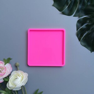 May include: A bright pink square silicone mould for resin crafts. The mould is on a grey background.