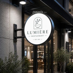 Pode incluir: Uma placa circular, iluminada e de dupla face em metal preto montada numa parede de pedra. A placa apresenta uma face branca com um logótipo preto de uma taça com uma planta, o texto LUMIÈRE RESTAURANT e EST. 2021 em letras pretas.
