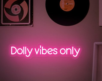 May include: A bright pink neon sign with the words "Dolly vibes only" illuminates a wall. The sign is the focal point, with a record player and vinyl records in the background. The sign is a decorative item.