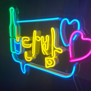 May include: Neon sign with the Korean word "Let's Drink" in yellow, surrounded by a blue outline. Two pink hearts are on the right side of the sign.