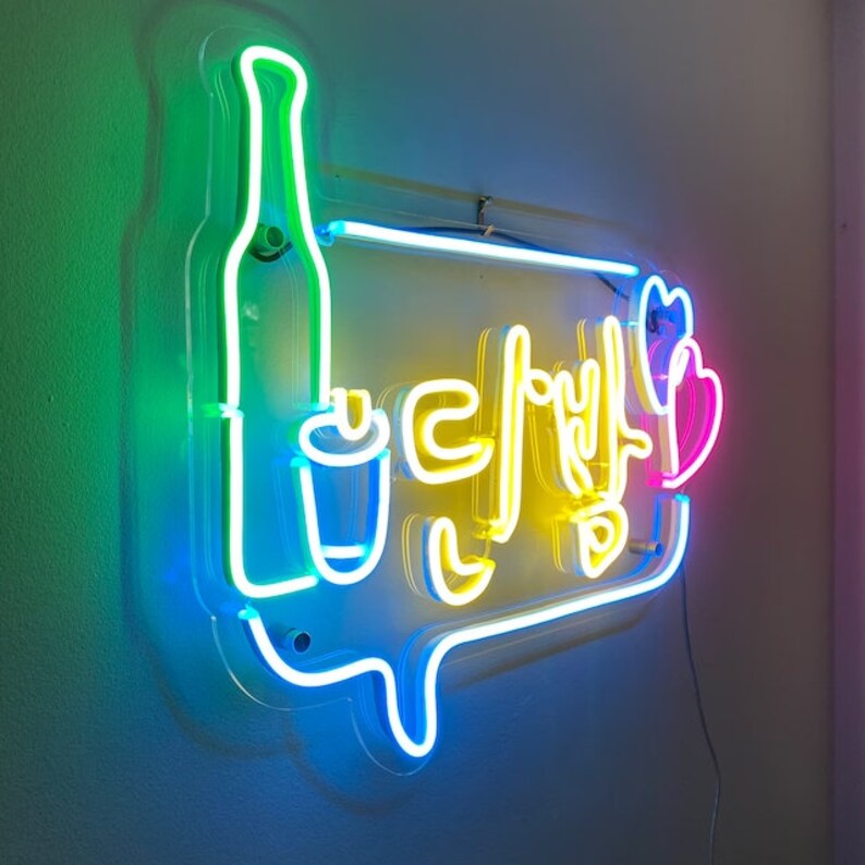 May include: Neon sign with a blue, green, and yellow outline. The sign says "다방" in Korean, which means "coffee shop". There is a stylized image of a bottle and a cup on the sign.