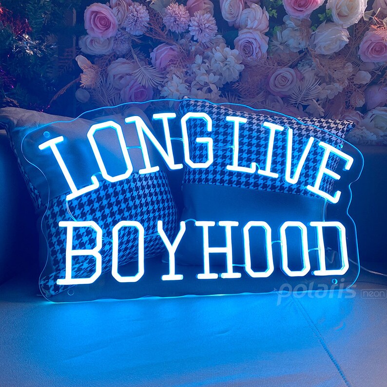 May include: A neon sign with a blue glow, shaped like a banner, with the words "Long Live Boyhood" in white neon letters.