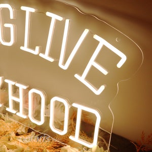 May include: White neon sign with the words "LIVE HOOD" on a clear acrylic background. The sign is sitting on a surface covered in dried flowers.