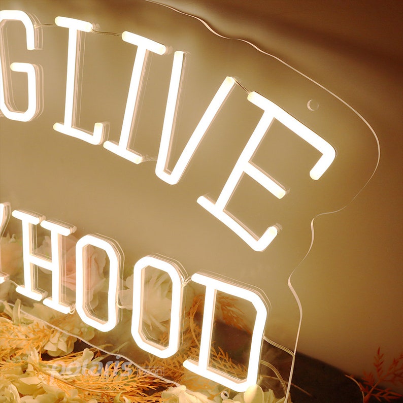 May include: White neon sign with the words "LIVE HOOD" on a clear acrylic background. The sign is sitting on a surface covered in dried flowers.