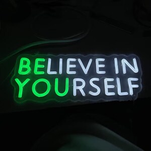 May include: Neon sign with the words "Believe in Yourself" in white and green neon lights.