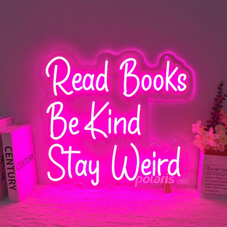 May include: Pink neon sign with the text "Read Books Be Kind Stay Weird" and the company name "polaris neon" in the bottom right corner.