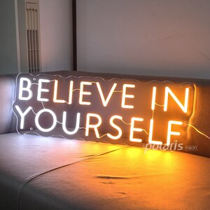 May include: White neon sign with the words "Believe in Yourself" in a wavy font. The sign is lit up with a warm yellow glow.