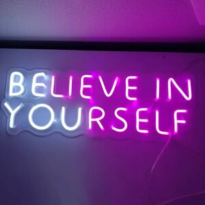 May include: Neon sign with the words "Believe in Yourself" in white and pink neon lights.
