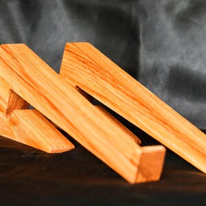 May include: Two wooden laptop stands made of light brown wood. The stands are angled to create a raised platform for a laptop.