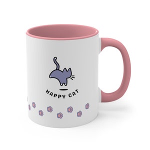 May include: White ceramic mug with a pink rim and handle. The mug features a cartoon illustration of a cat with the text "HAPPY CAT" below it. A row of pink paw prints are at the bottom of the mug.