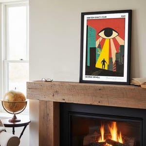 May include: Framed art print of a retro-style illustration for George Orwell's "Nineteen Eighty-Four." The artwork features a large eye, a figure, and city buildings in a vibrant color palette of red, yellow, and teal. The print is displayed above a fireplace.