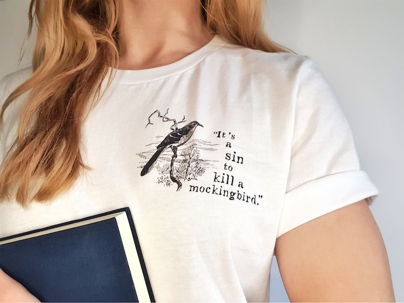May include: White t-shirt featuring a black and white illustration of a mockingbird and the text "It's a sin to kill a mockingbird."