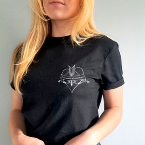 Puede incluir: Camiseta negra con mangas enrolladas. La camiseta presenta un gr&aacute;fico blanco de un coraz&oacute;n atravesado por una flecha, con el texto "I am made of memories" en una pancarta. La camiseta est&aacute; hecha de un material suave.