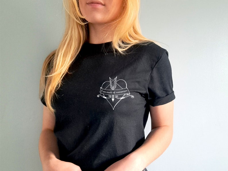 Puede incluir: Camiseta negra con mangas enrolladas. La camiseta presenta un gr&aacute;fico blanco de un coraz&oacute;n atravesado por una flecha, con el texto "I am made of memories" en una pancarta. La camiseta est&aacute; hecha de un material suave.