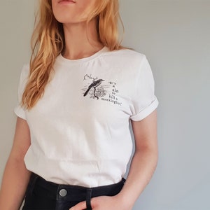 May include: White t-shirt with a black and white illustration of a bird and the text "It's a sin to kill a mockingbird."