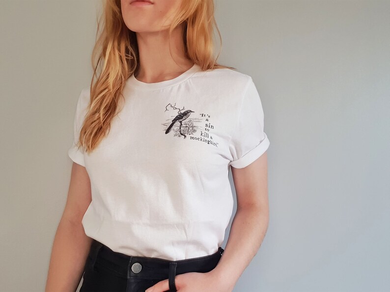May include: White t-shirt with a black and white illustration of a bird and the text "It's a sin to kill a mockingbird."