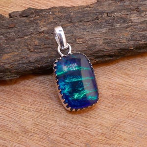 Może przedstawiać: Srebrny wisiorek z niebiesko-zielonym opalem. Opal jest osadzony w srebrnej oprawie z falistym brzegiem.
