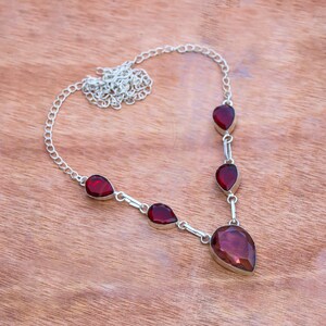 May include: A silver chain necklace with five teardrop-shaped red gemstones. The largest gemstone is at the bottom of the necklace and is a darker shade of red.