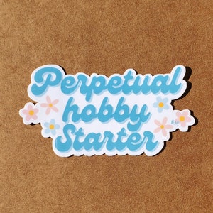 May include: A blue and white sticker with the text "Perpetual hobby starter" in a retro font. The sticker is decorated with small pink and blue flowers.