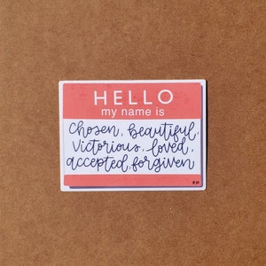 May include: A pink and white name tag sticker with the text "HELLO my name is chosen, beautiful, victorious, loved, accepted, forgiven".