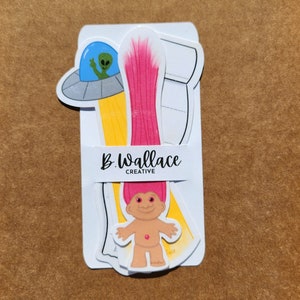 May include: A set of three paper craft cutouts featuring a pink-haired troll, a yellow spaceship with a green alien, and a white background with the text "B. Wallace Creative".