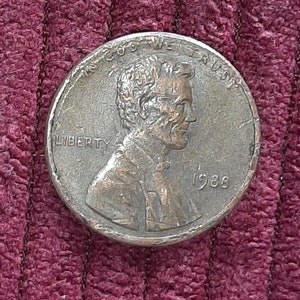 Puede incluir: Una moneda de un centavo estadounidense de cobre de 1988 con las palabras "LIBERTY" e "IN GOD WE TRUST" y el año "1988" visibles.