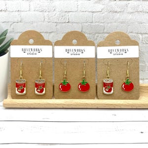 May include: Three pairs of gold dangle earrings with red tomato and tomato can charms. The earrings are displayed on brown card stock with the text "ROVEWORKS STUDIO" printed on each card.
