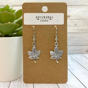 May include: Silver maple leaf dangle earrings on a brown card with the text "ROVEWORKS STUDIO".