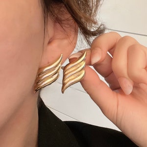 May include: Gold tone earrings with a wing design. The earrings are made of metal and have a shiny finish.