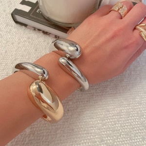 May include: Two silver and gold bangle bracelets with a unique abstract design. The bracelets are worn on a person's wrist.