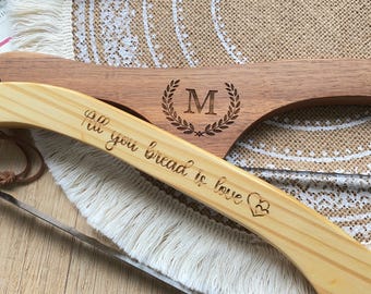 May include: Two wooden bread slicers. One is light-colored with the text "All you bread is love" and a heart symbol. The other is dark-colored with the letter "M" inside a laurel wreath. Both have a curved handle.