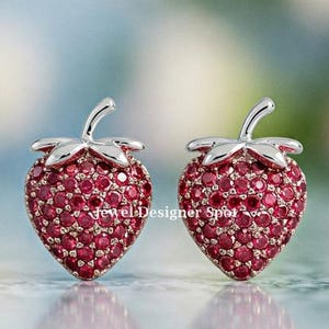 以下が含まれることがあります： 赤いキュービックジルコニアの石がついたイチゴの形をしたシルバーのイヤリングのペアです。