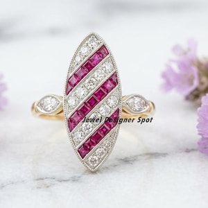 May include: A gold and silver ring with an elongated oval design. The ring features alternating rows of small, square, red and white stones. The ring has a gold band and small, decorative stones on either side of the oval.