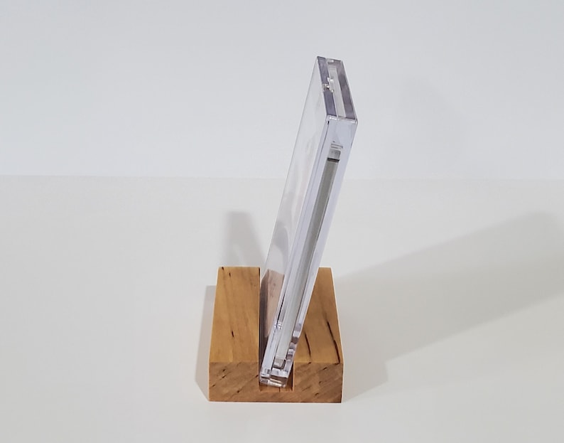 May include: A clear plastic display stand with a wooden base. The stand is designed to hold a CD or DVD case.