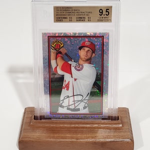 Puede incluir: Una tarjeta de béisbol de Bryce Harper con el uniforme de los Nacionales de Washington, calificada con 9.5, en un soporte transparente. La tarjeta se muestra en un soporte de madera. El texto de la tarjeta dice "2014 Bowman" y "Silver Diamond Refractors".