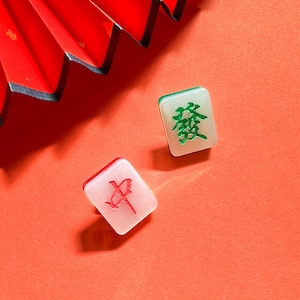 Puede incluir: Dos fichas de mahjong blancas con caracteres chinos sobre un fondo rojo. La ficha de la izquierda tiene un carácter rojo, y la ficha de la derecha tiene un carácter verde.