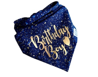Pode incluir: Uma bandana triangular para animal de estimação em azul-marinho profundo com um padrão salpicado de pontos azul-claros e dourados. O texto Birthday Boy está impresso em fonte cursiva dourada metálica, com um pequeno balão dourado ao lado.