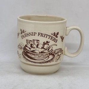 May include: A white ceramic mug with a brown illustration of a bowl of parsnip fritters. The mug has a brown handle and the text "Parsnip Fritters" is printed on the side.